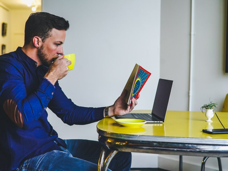 man drinking on yellow cup while reading book